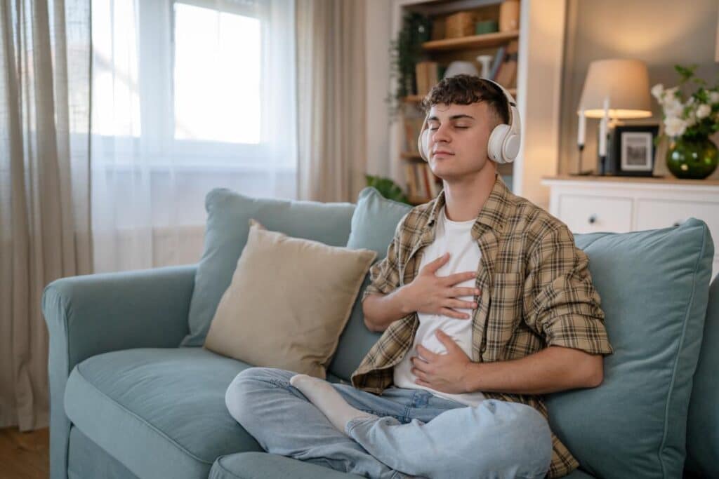 teenage boy sitting on couch listening to music with headphones as one of 5 self-care activities to help depression