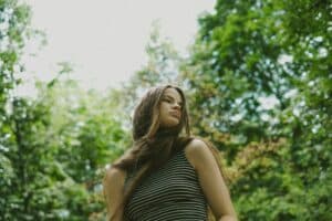 teen girl standing in the woods alone looking off into the trees